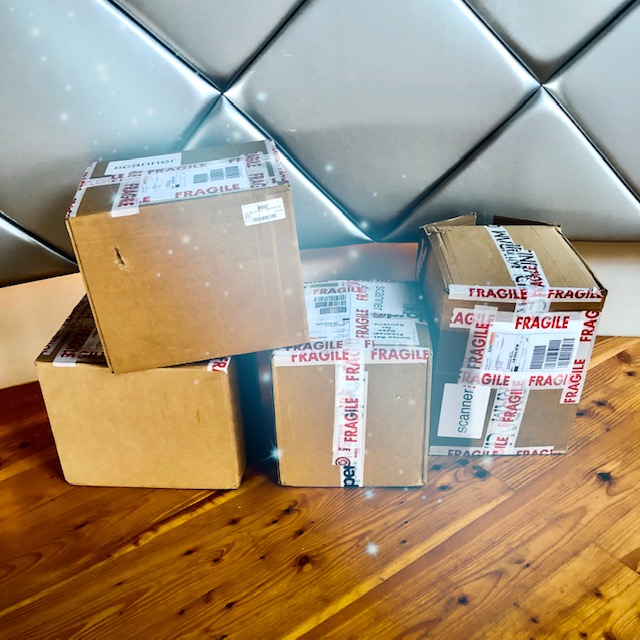 Four large cardboard boxes on the floor, covered in fragile tape. They look heavy and filled to the surface with records and CDs.