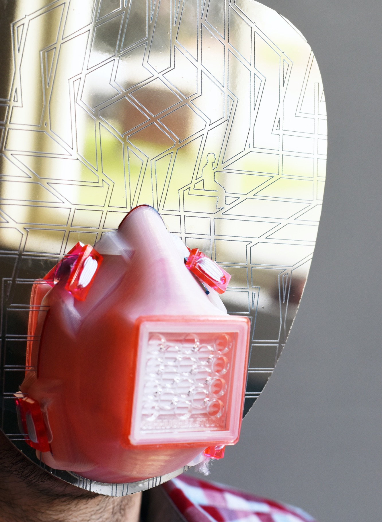 A mask, shiny flat surface, with lines etched all over it, with a red plastic filter over the mouth area